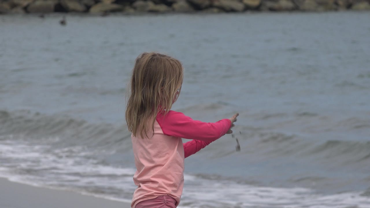 Young girl in pink extending her arm toward the waves.