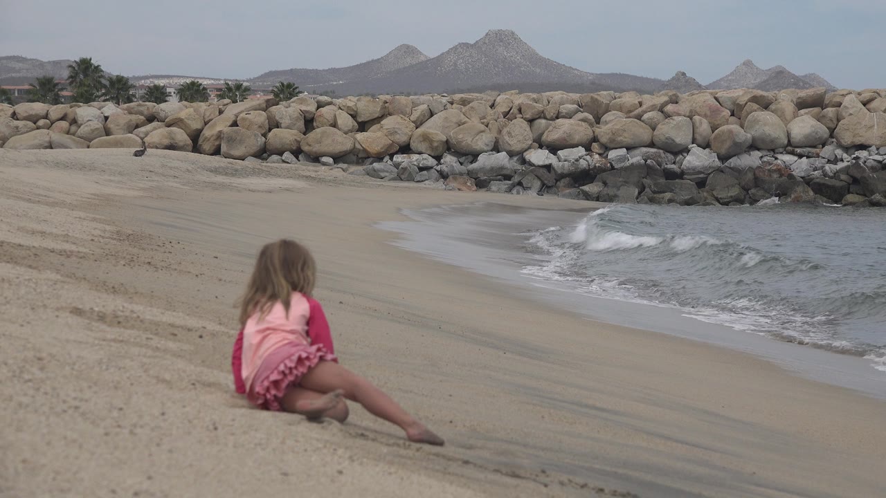 Girl sitting near a breaking wave on an empty beach.