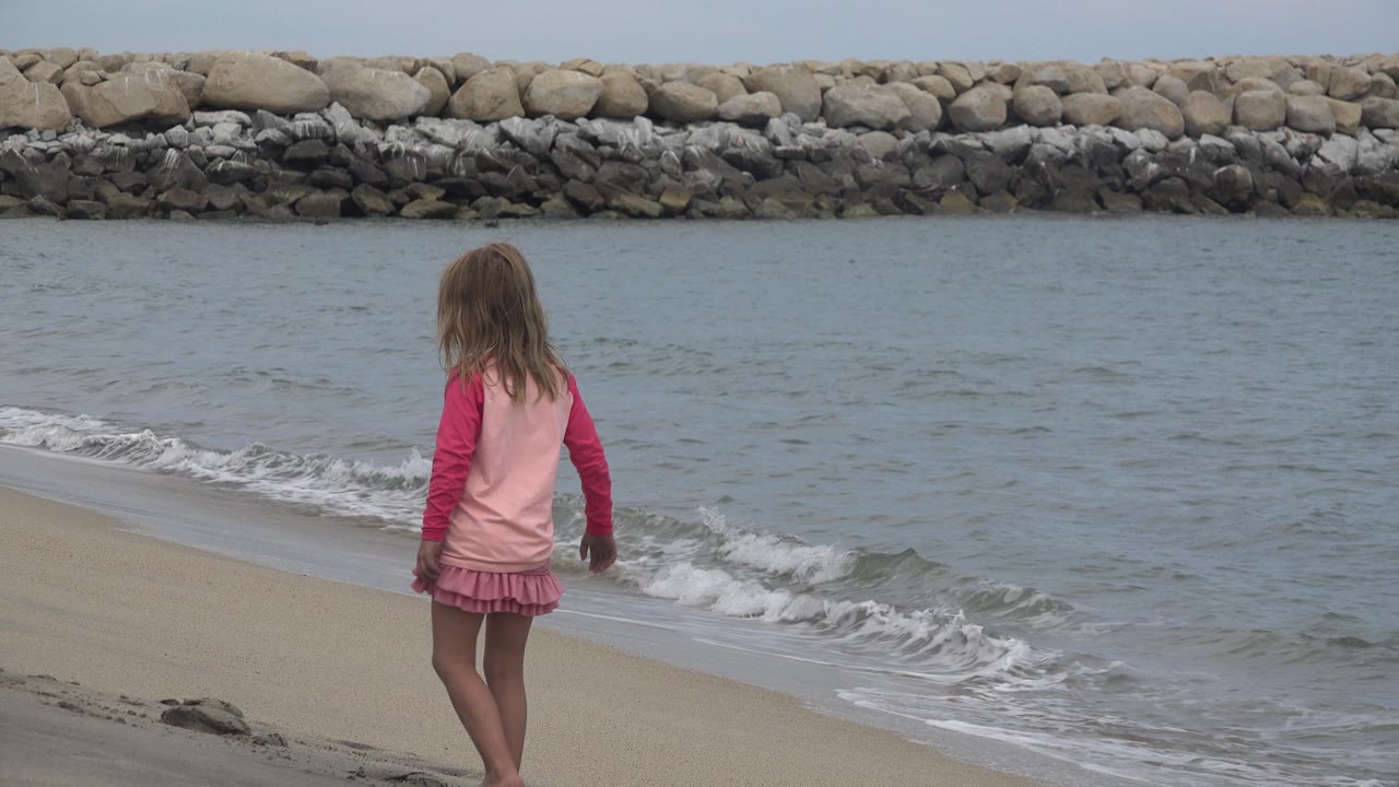 Girl walking along the sandy beach near a small breaking wave.