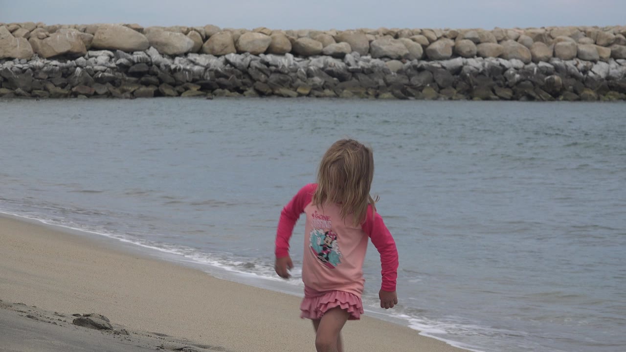 Young girl in a pink frilly dress walking near the waterline.