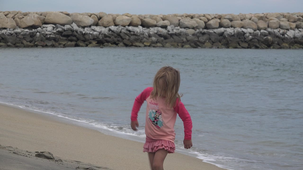 The child continues along the San Jose del Cabo beach, angled slightly toward the water as the low surf reaches the sand behind her.