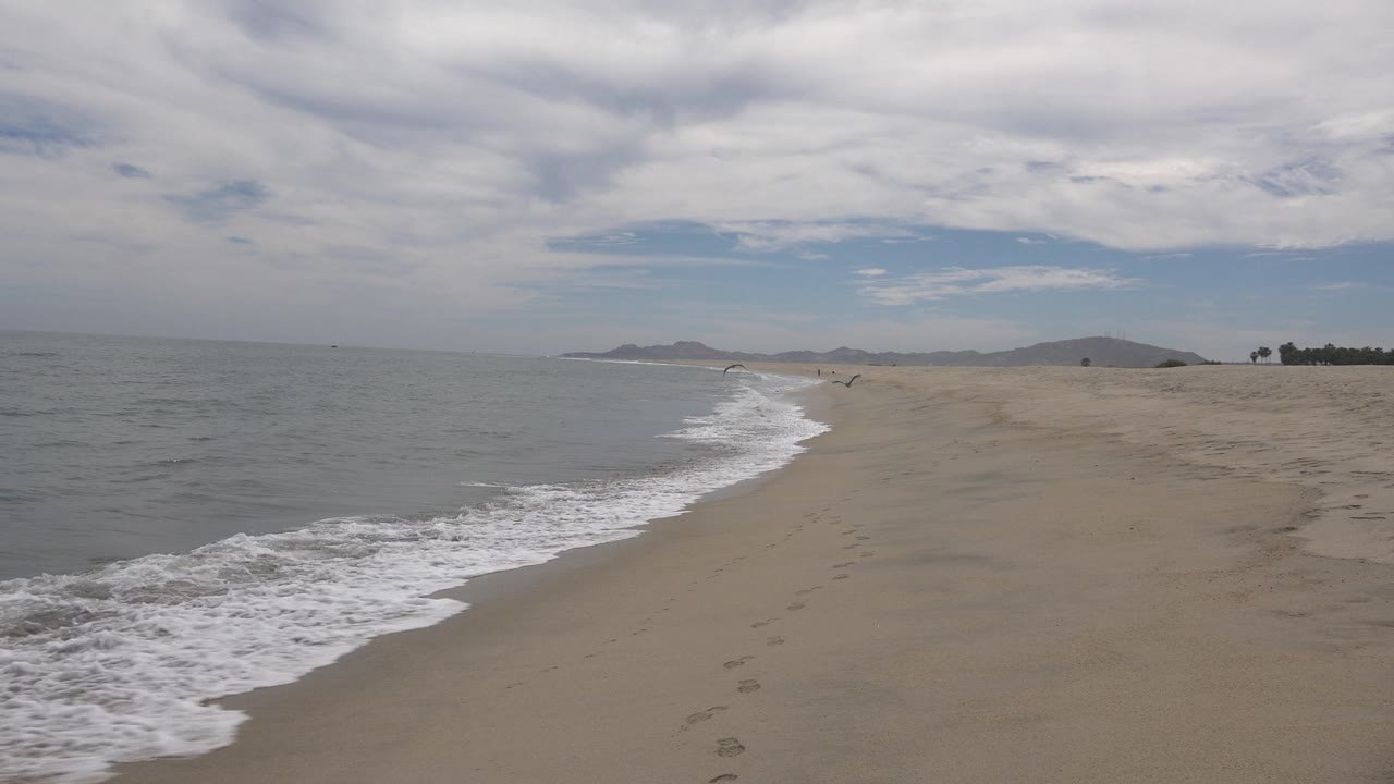 Curving surf line on an empty beach with distant hills.