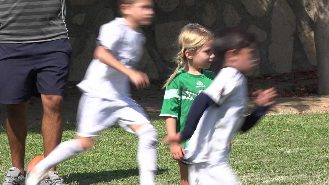One second into the San Jose del Cabo, Mexico clip, two white-uniformed children run across the foreground while the girl in green remains near the center of the grass field.