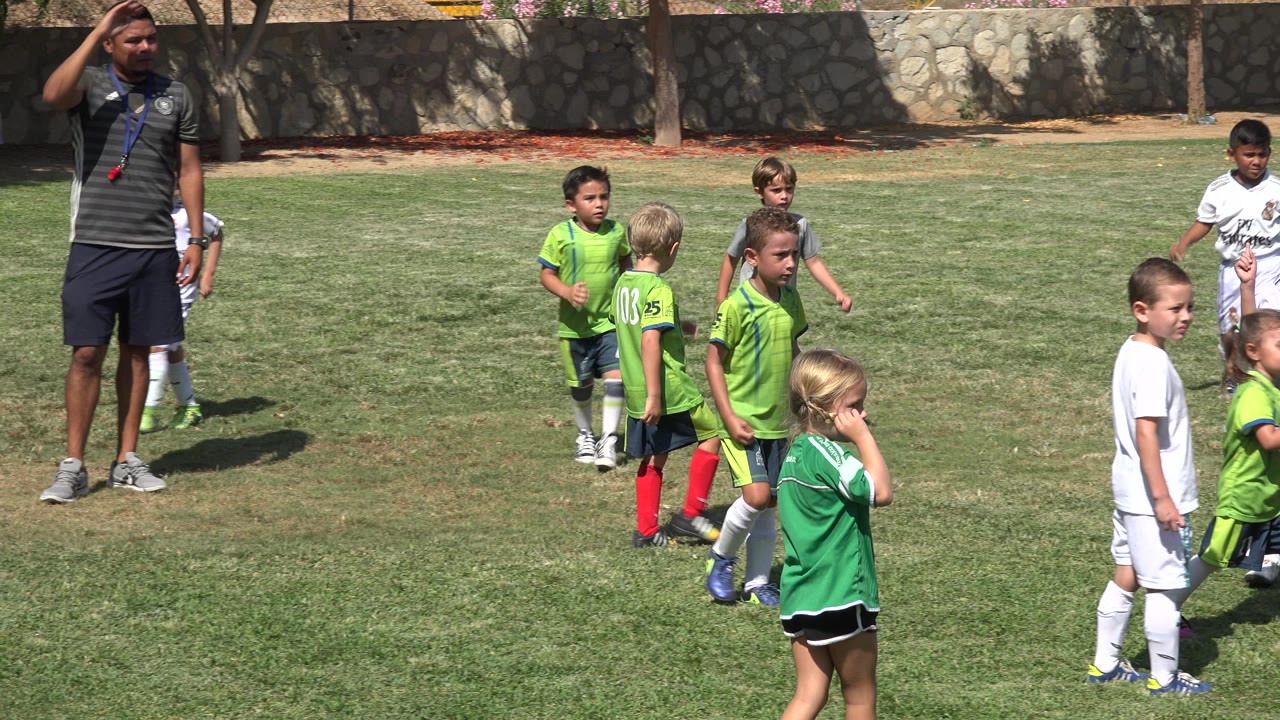 A cluster of children in green and white soccer kits stands on the field in San Jose del Cabo, Mexico, with the coach still visible near the right side.