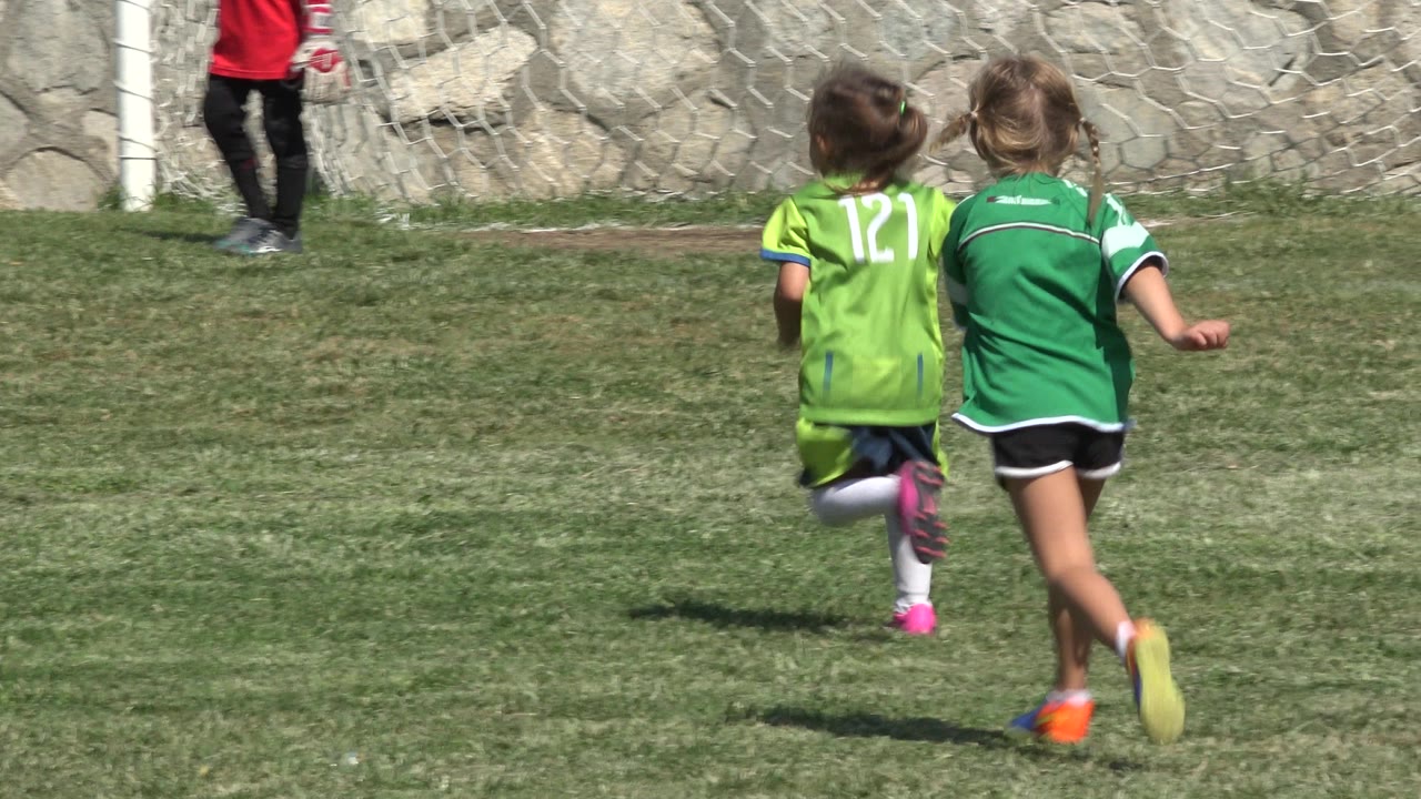 The two children in green jerseys move farther across the sunlit soccer field in San Jose Del Cabo, Mexico, with their backs mostly facing the camera.