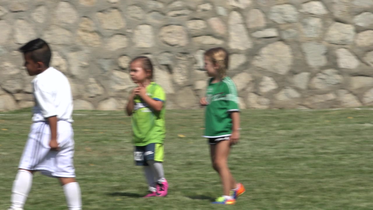 A boy in a white uniform and two children in green uniforms move in profile across the grass in San Jose del Cabo, Mexico.