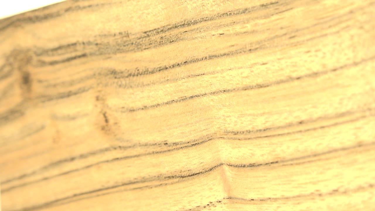 The wood surface remains close to camera, with darker horizontal grain bands crossing a warm pale slab and no visible people.