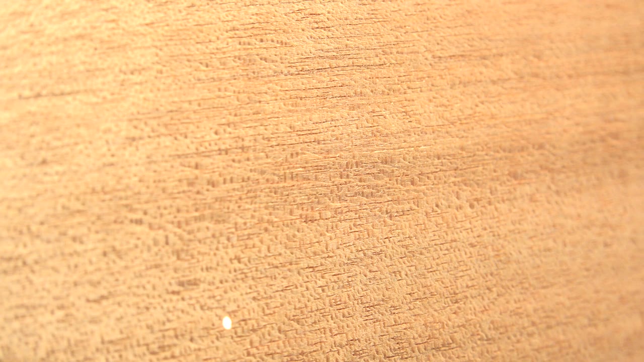 Close view of tan wood grain at the start of the Westminster, Colorado clip, with a small bright speck near the lower left and no visible people.