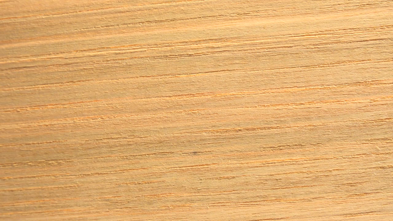 A similar close wood surface appears one second in, with horizontal grain lines and a slightly brighter tan cast, with no visible people.