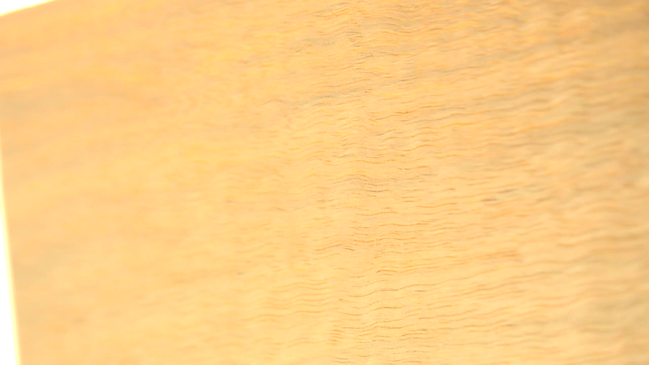 A close view of yellow plywood in Westminster, Colorado, with fine wood grain, a bright vertical glare along the left edge, and no visible people.