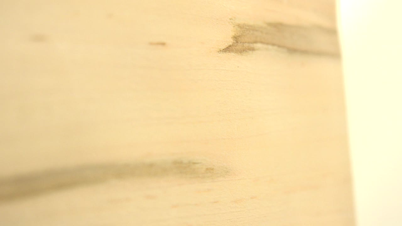 Close view of a tan wooden board in Westminster, Colorado, with a dark grain streak near the top and a bright vertical edge at right, with no visible people.