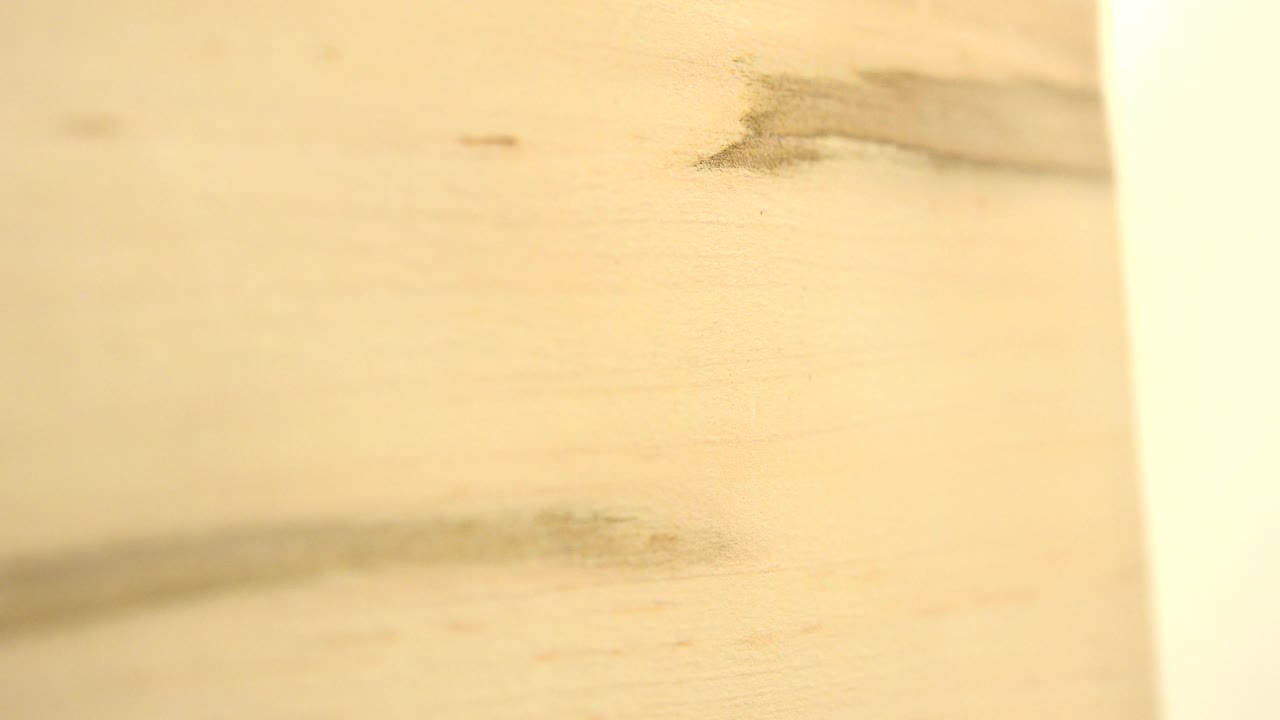 The board remains in close-up in Westminster, Colorado, with soft tan grain, a dark smudge near the lower left, and a bright vertical strip on the right, with no visible people.