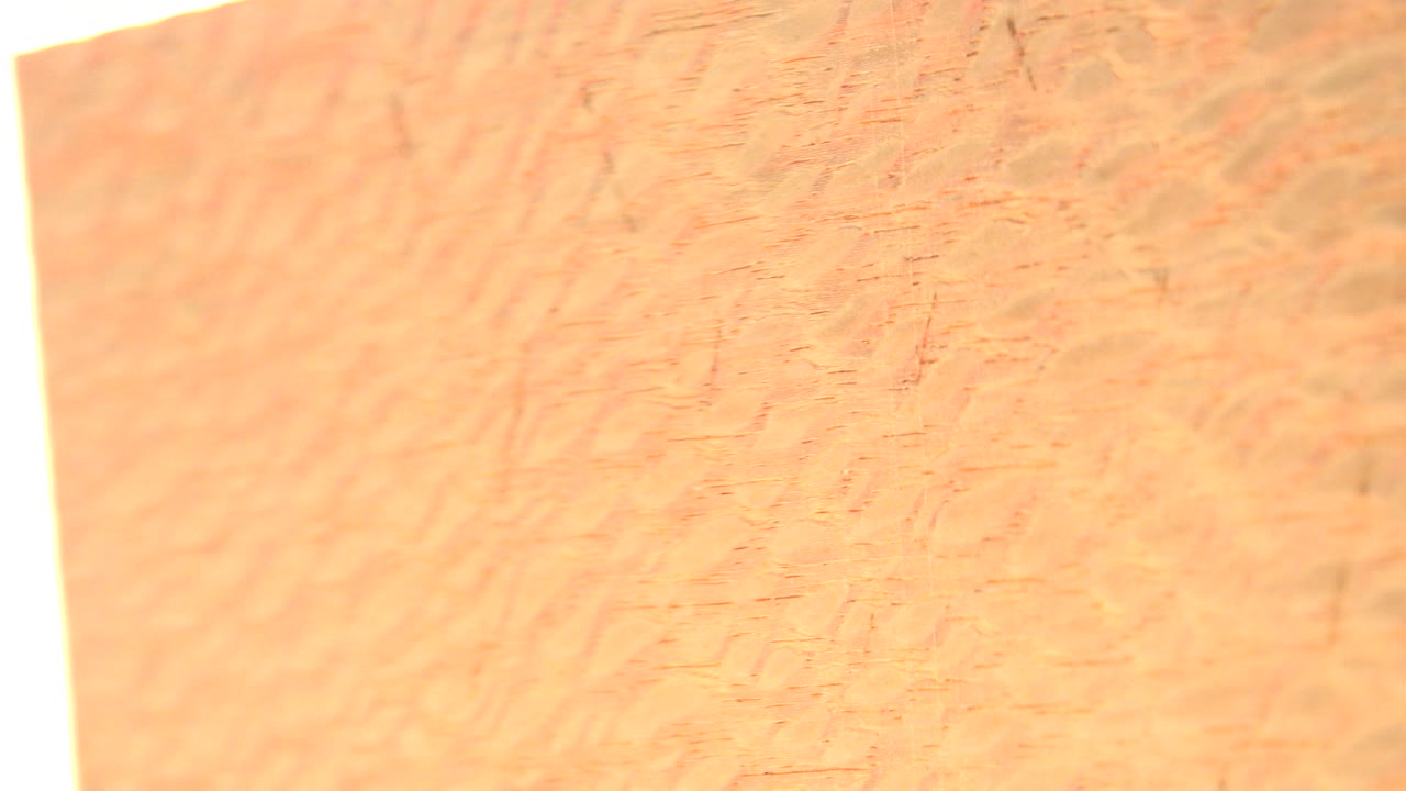 At 0:01, the gold-colored object remains in tight close-up with a pale vertical edge at left and no visible people.