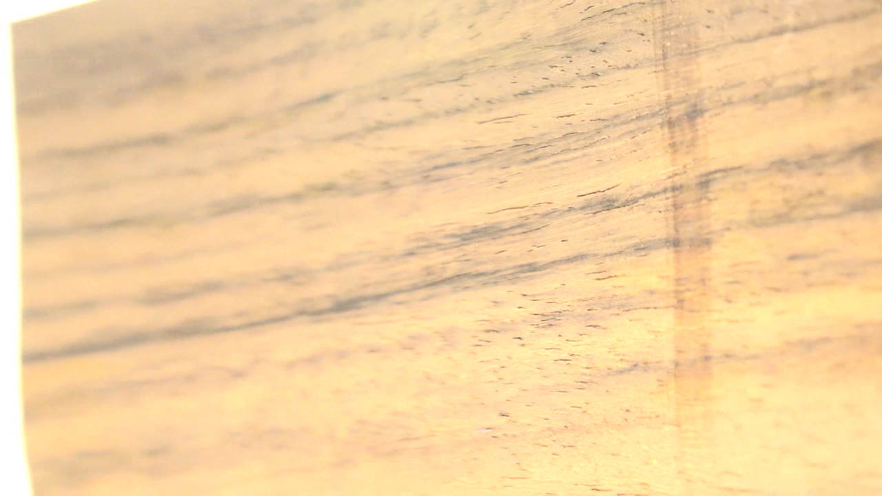 At 0:00, a close view of a thin wood slice in Westminster, Colorado shows warm horizontal grain with a bright white glow along the left edge and no visible people.