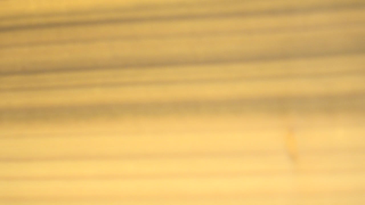 At 0:01, the tan wooden board remains soft and blurred while a bright vertical white band appears along the right side, with no visible people.
