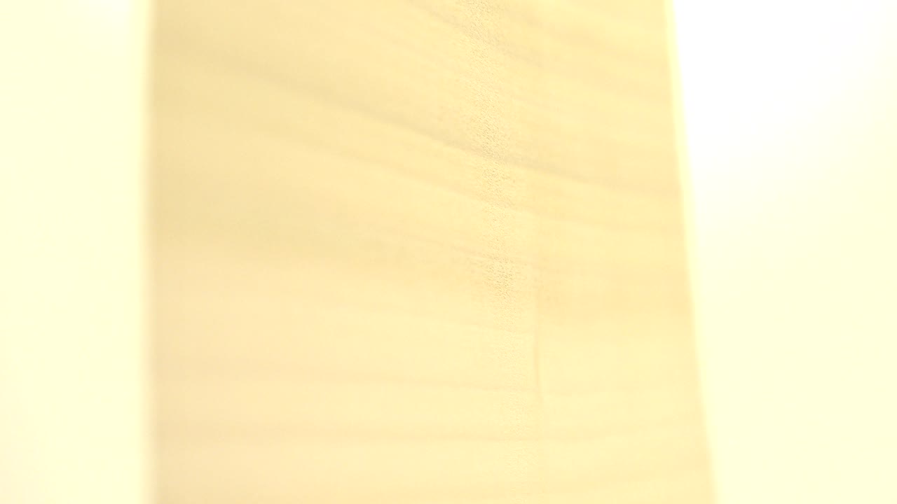 At 0:01, the yellow object is partly washed out by a tall white glare band over the wood-grain background in Westminster, Colorado, with no visible people.