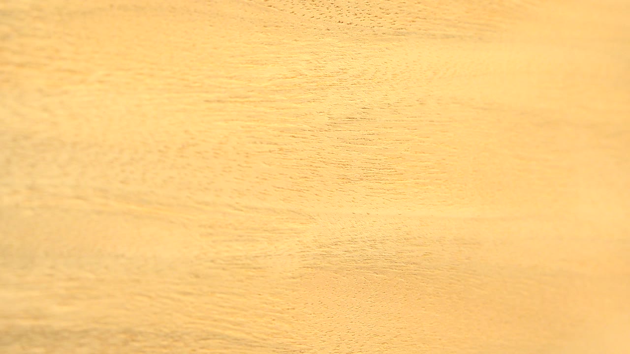 Close-up tan wood board surface in Westminster, Colorado, with fine horizontal grain lines and no visible people at the start of the clip.