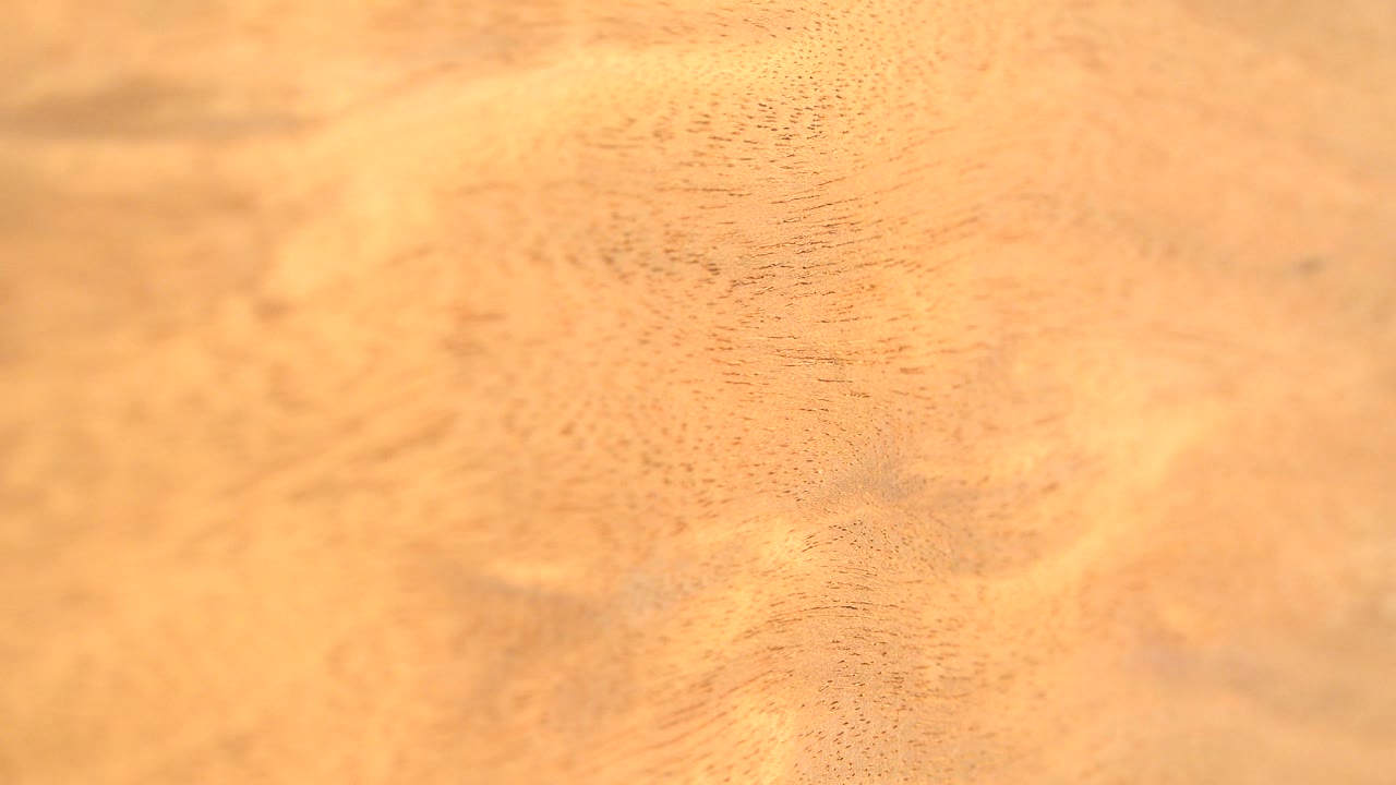 A warmer, softer view of the rotating wood surface shows faint darker grain marks across the frame, with no visible people.