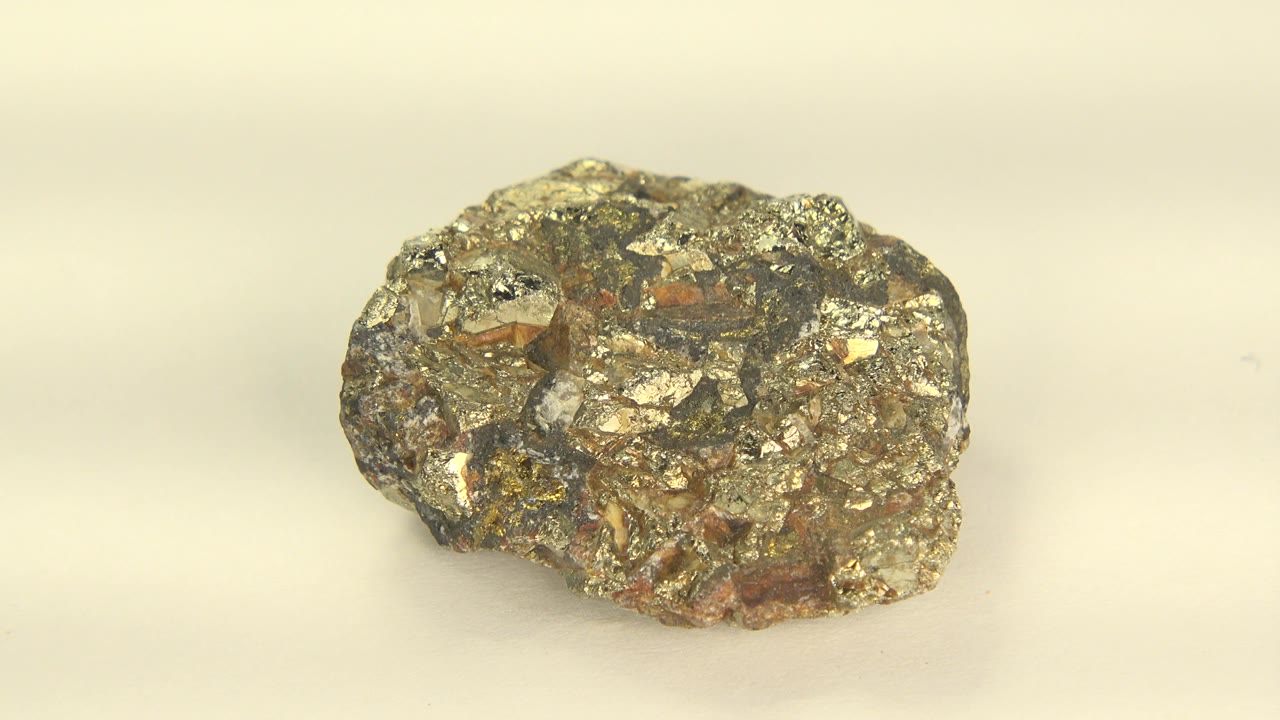 A rough golden stone rests near center frame on a pale pink cream surface in Westminster, Colorado footage, with small metallic highlights and no visible people.
