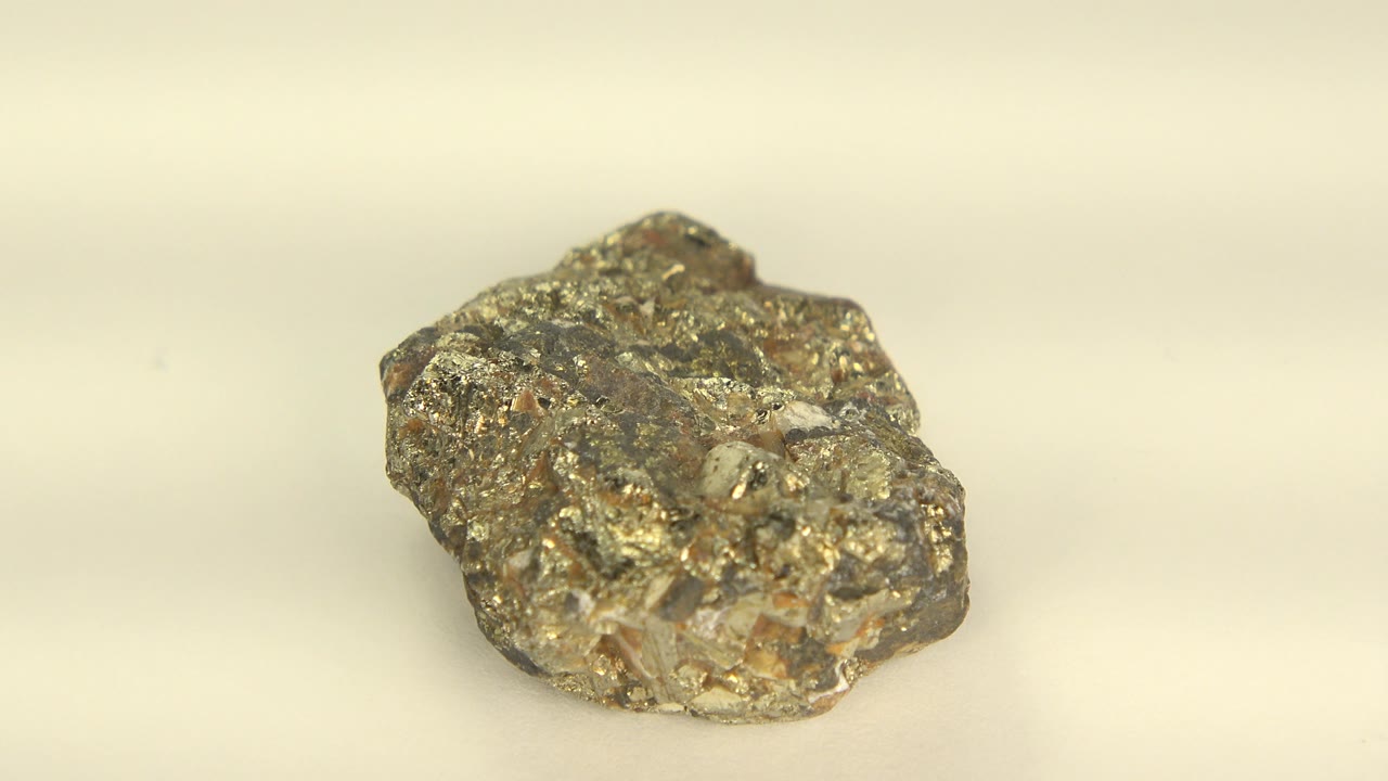 A gold-colored rough mineral specimen rests on a pale display surface in Westminster, Colorado, with warm highlights on its metallic flecks and no visible people.