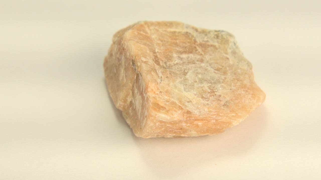 Yellow-orange sandstone rock seen in close-up on a pale surface in Westminster, Colorado footage, with its broad top face angled toward camera and no visible people.