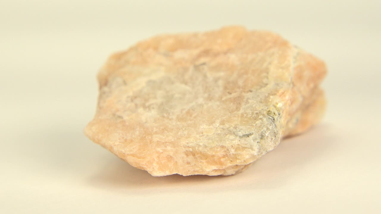 At 0:00, a peach-pink and white rock rests low on a white floor in Westminster, Colorado, with soft focus and no visible people.