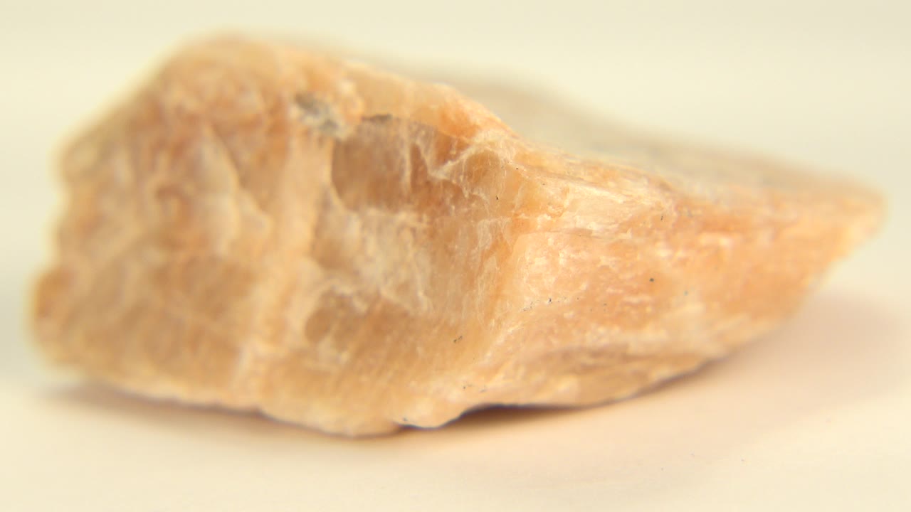 Close view of a peach and tan rock resting on pale sand in Westminster, Colorado, with shallow focus and no visible people.