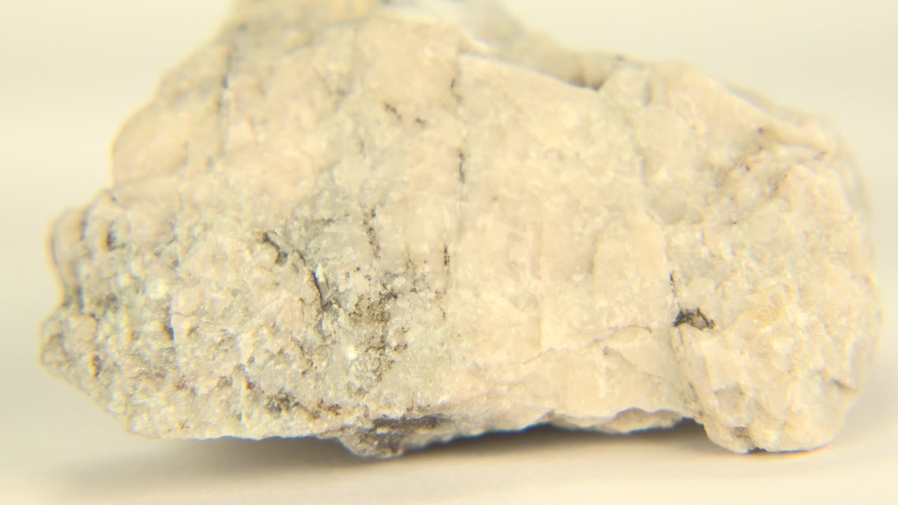 The pale powdery rock has turned slightly on the tabletop, showing more of its rough lower edge and gray-speckled face, with no visible people.
