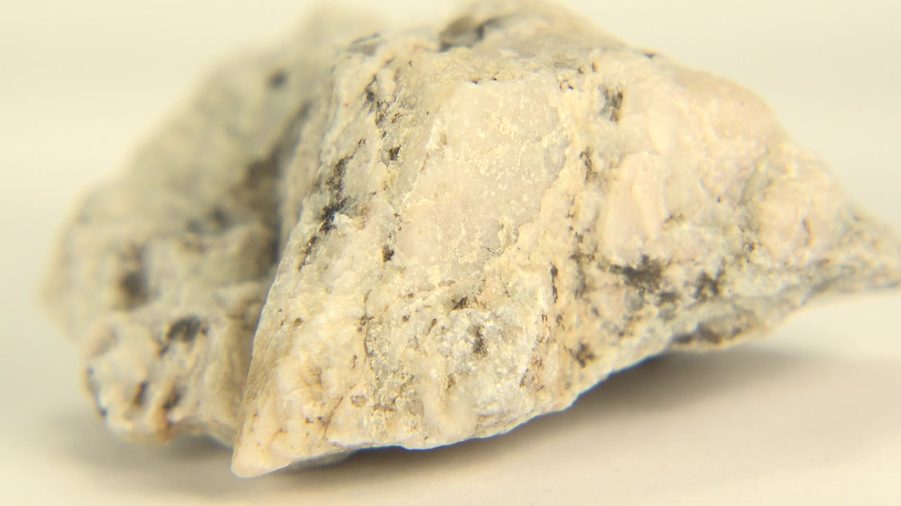 The quartz rock remains close to the lens, showing a broad white face, dark flecks, and a small pointed edge against a pale background in Westminster, Colorado, with no visible people.