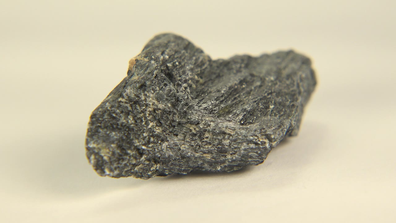 The black granite rock remains centered on the pale floor in Westminster, Colorado, with a slightly shifted view of its layered gray texture and no visible people.