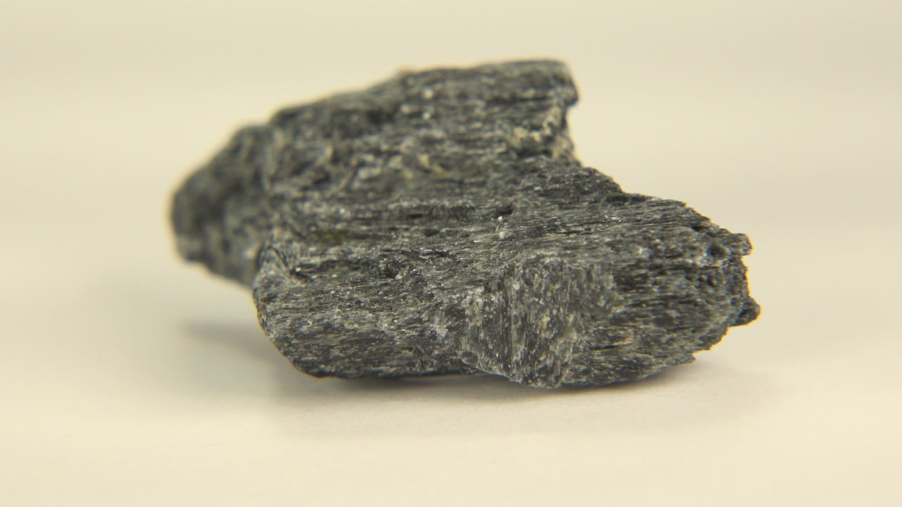 Rough dark stone centered in a close macro composition, showing ridges and small pits on a cream surface in Westminster, Colorado, with no visible people.