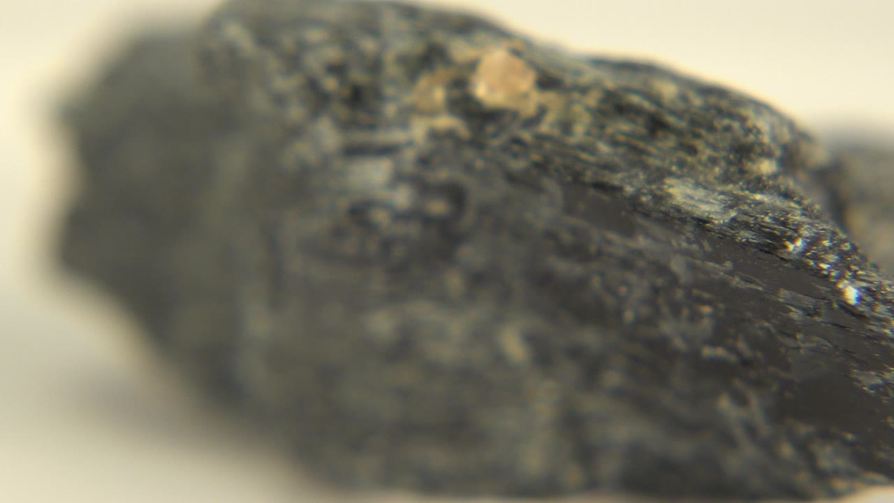 Soft macro view of a dark shiny rock on a pale surface.