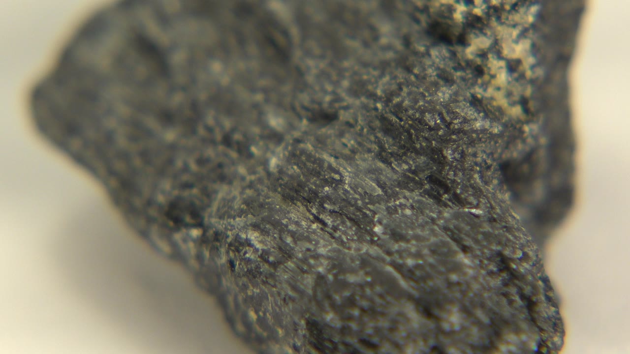 A dark gray rock surface fills the frame in Westminster, Colorado footage, with a pointed lower edge, shallow focus, warm pale background, and no visible people.