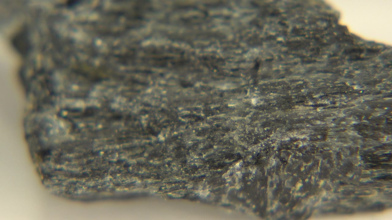 Close-up of a dark gray rough-edged stone or black glass fragment on a pale floor in Westminster, Colorado, with no visible people.