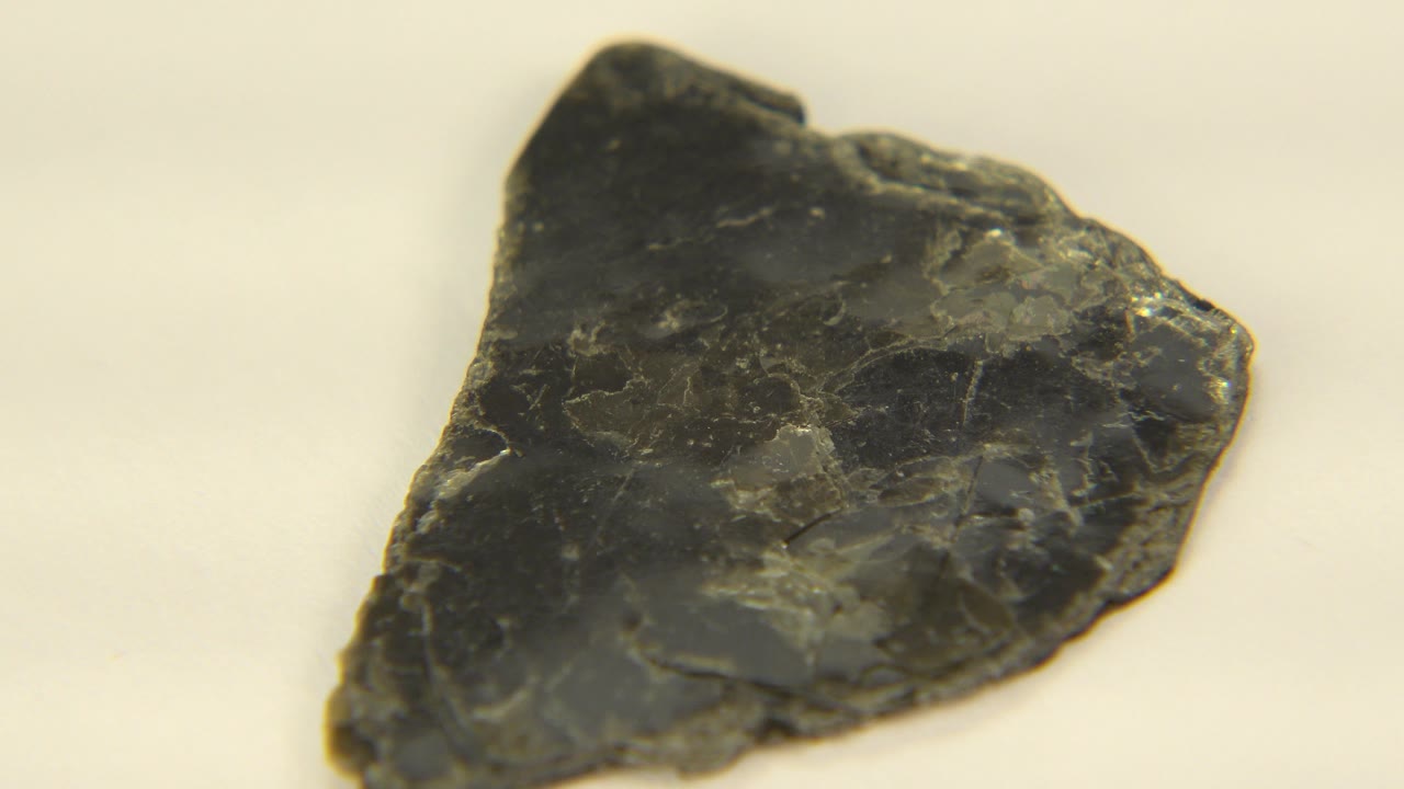 The black rock remains centered on the white surface, showing pale veins and glossy patches, with no visible people.