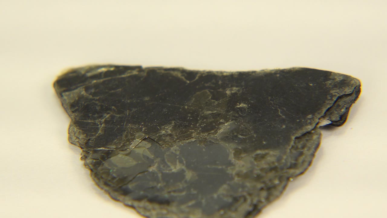 Close-up of a dark triangular shale fragment on a pale surface in Westminster, Colorado, with layered edges and no visible people.