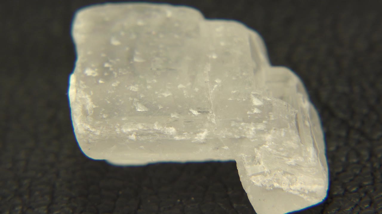 One second in, the white rock remains close to the camera on the dark table as its right edge begins to angle toward view, with no visible people.