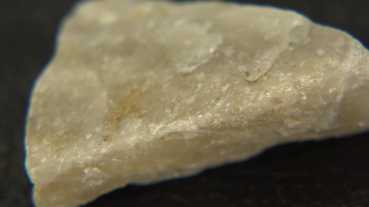 Close view of the yellow stone's rough side face on a dark tabletop in Westminster, Colorado, with tan streaks and no visible people.