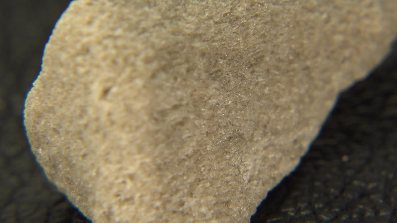 Close view of a pale yellow rough stone angled across a dark pebbled surface in Westminster, Colorado, with no visible people.
