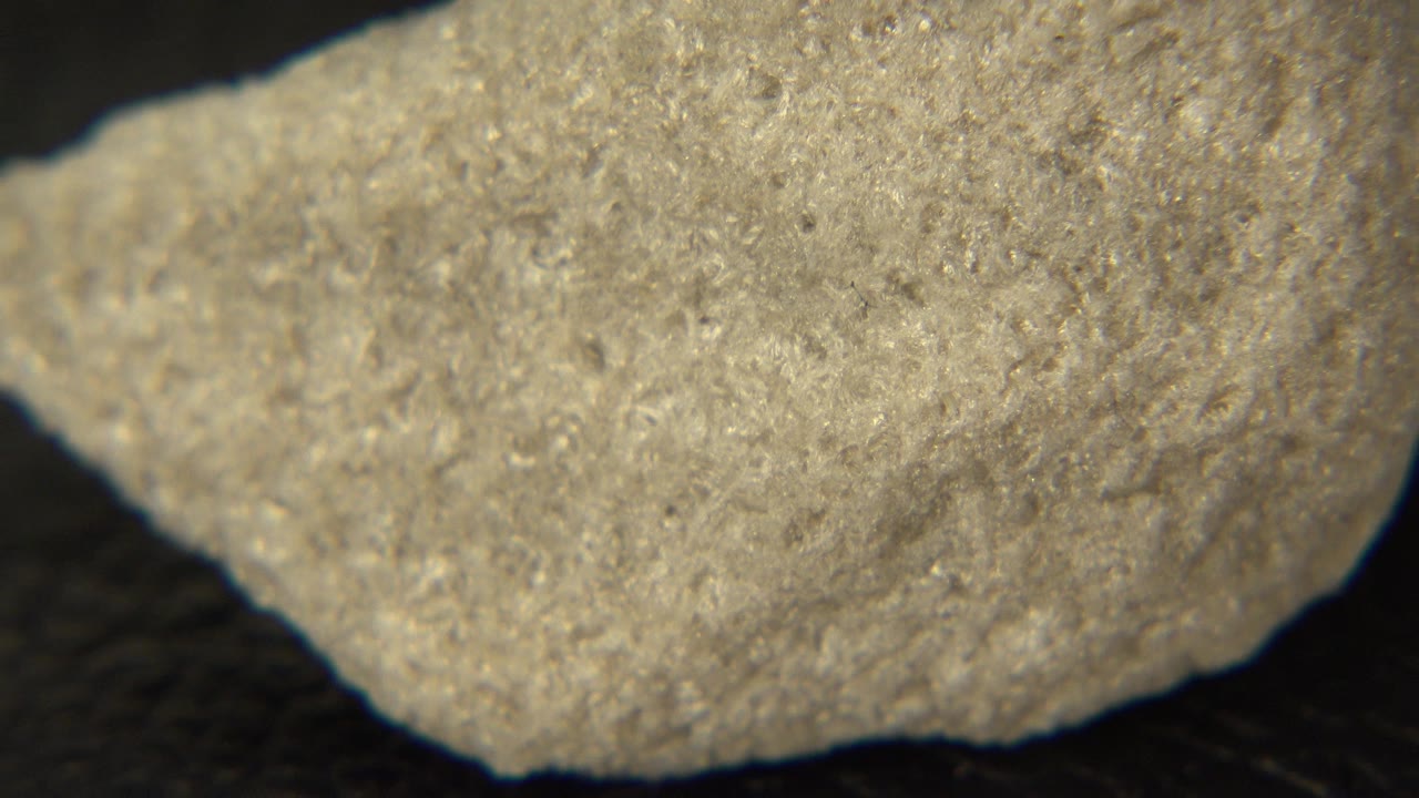 A pale gray rough rock fills the upper frame in Westminster, Colorado footage, with its lower edge visible against a dark textured background and no visible people.
