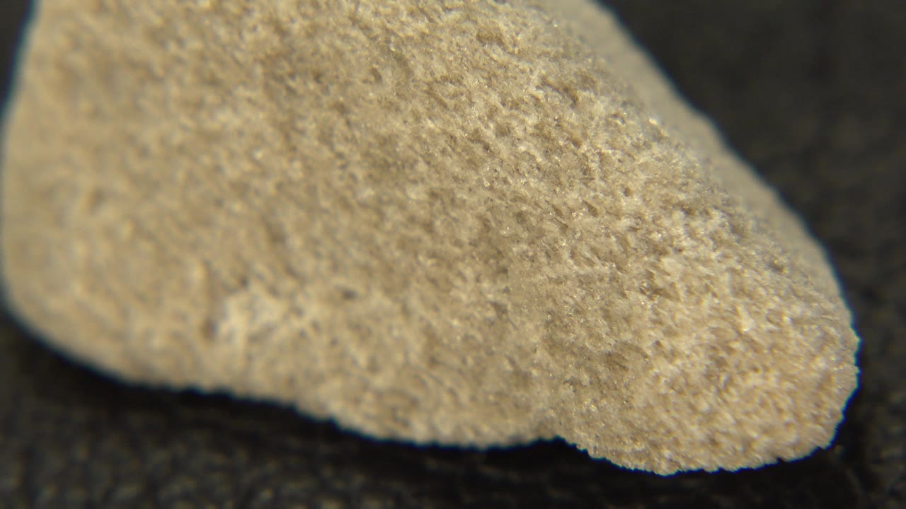 Close-up frame from Westminster, Colorado showing the rounded end of a tan rough rock on a dark surface, with no visible people.