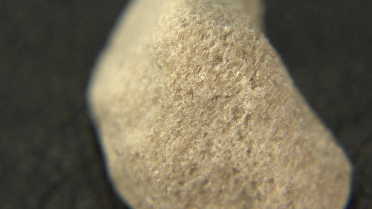 At 0:01, the rock appears slightly turned, showing a rounded off-white face with granular texture and no visible people.