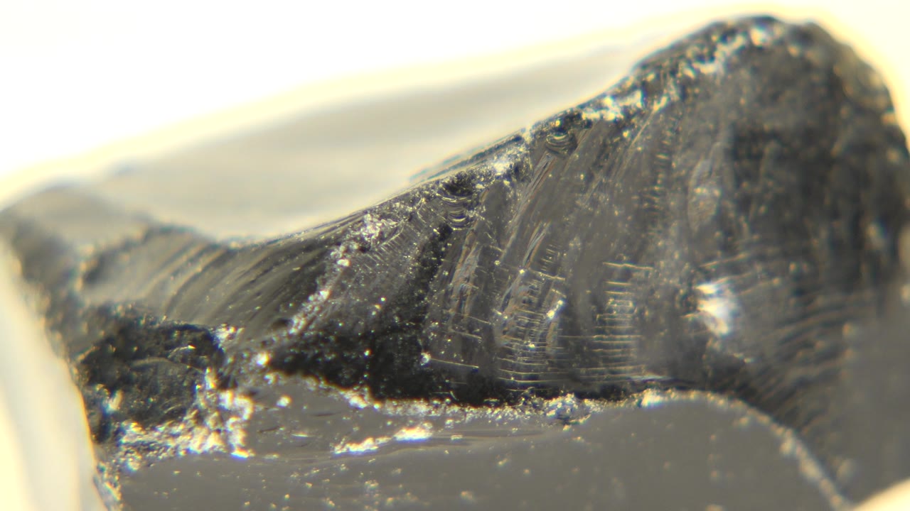 The granite piece remains tight in frame, showing a sloped black face, pale dust at the lower edge, soft focus behind it, and no visible people.