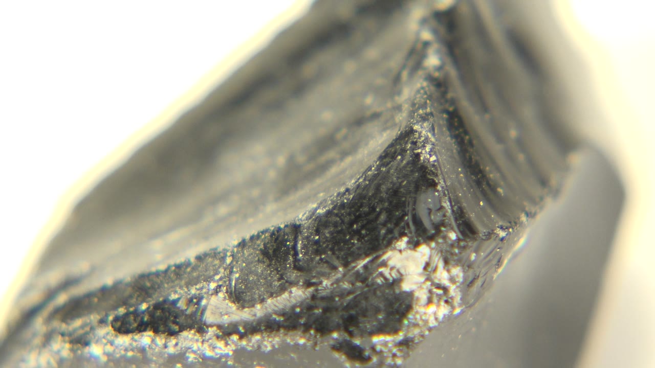 Macro close-up of a dark gray chipped stone edge on a pale background.