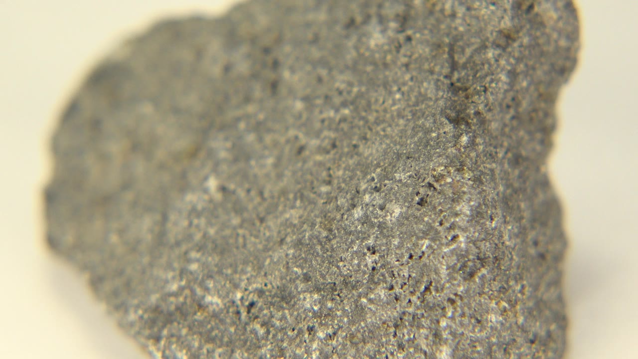 Close view of a gray speckled stone in Westminster, Colorado, with a rounded left edge, pale background, shallow focus, and no visible people.