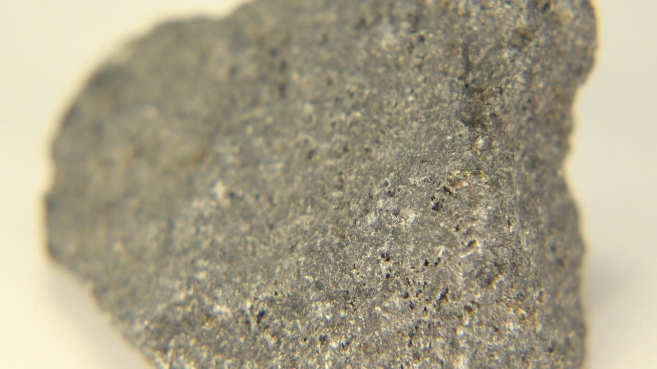 A gray rock face fills more of the center in Westminster, Colorado, with tiny white flecks, dark pores, a soft pale backdrop, and no visible people.