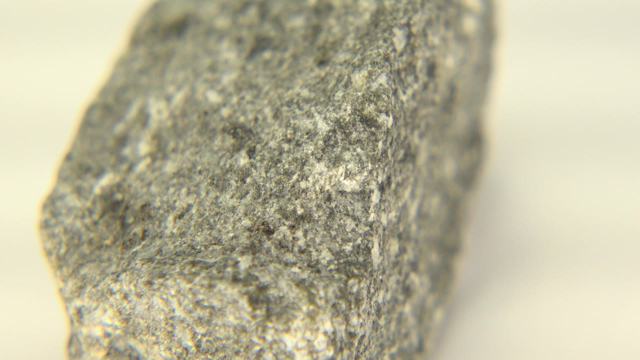 At 0:01, the gray stone fragment appears more centered in the macro view from Westminster, Colorado, with granular flecks visible on the front face and no visible people.