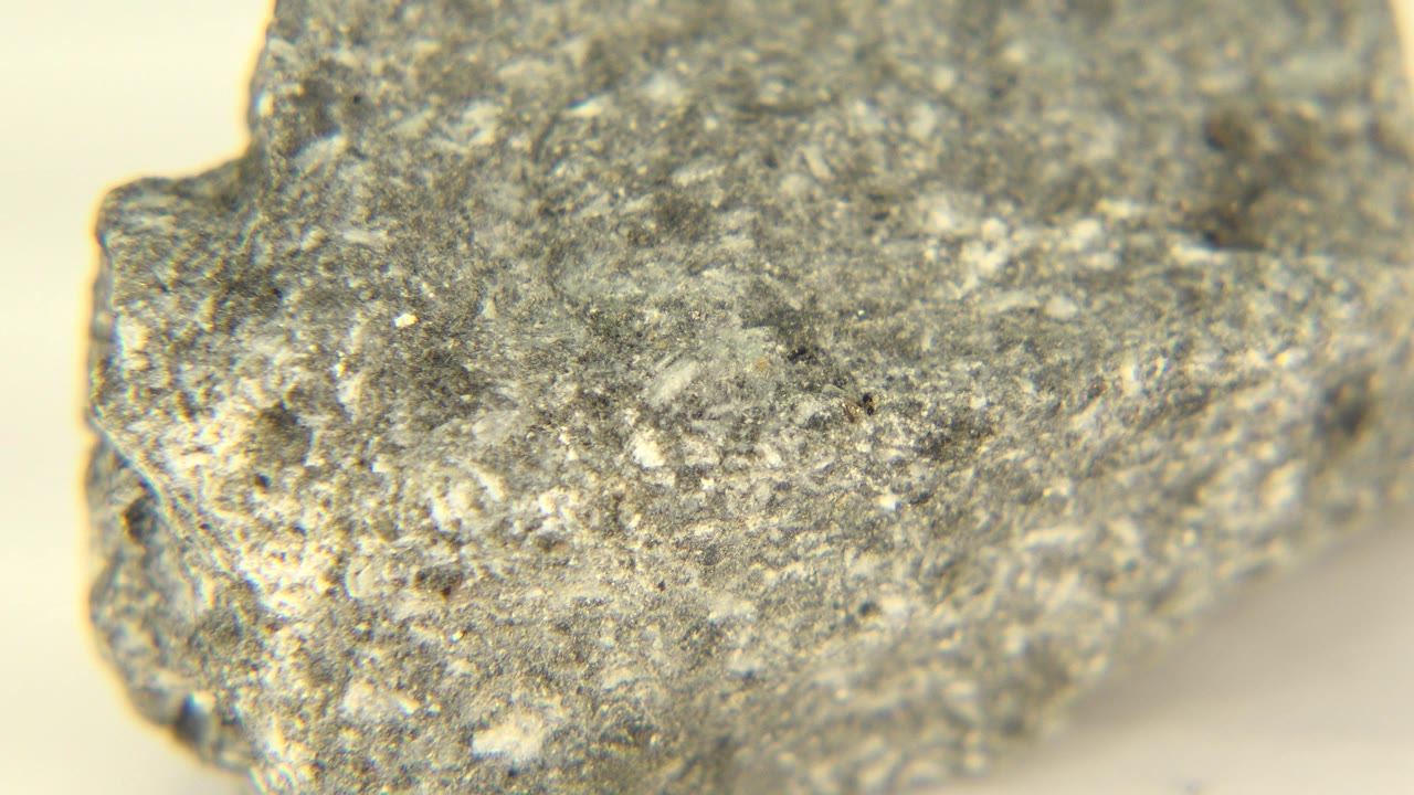 The mineral remains close to camera in Westminster, Colorado, showing a speckled gray top plane, chipped side edge, warm light, and no visible people.