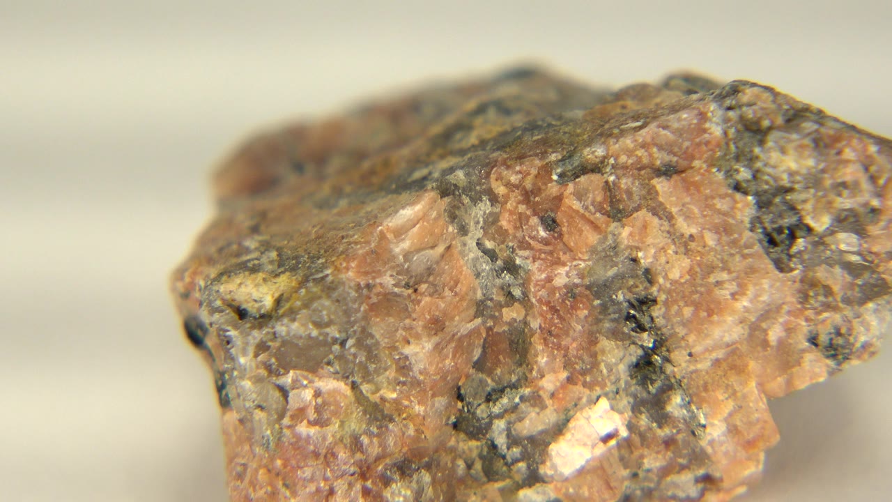 The red and dark mineral rock remains close to camera on the pale table, with a small bright fleck visible near the lower center and no visible people.