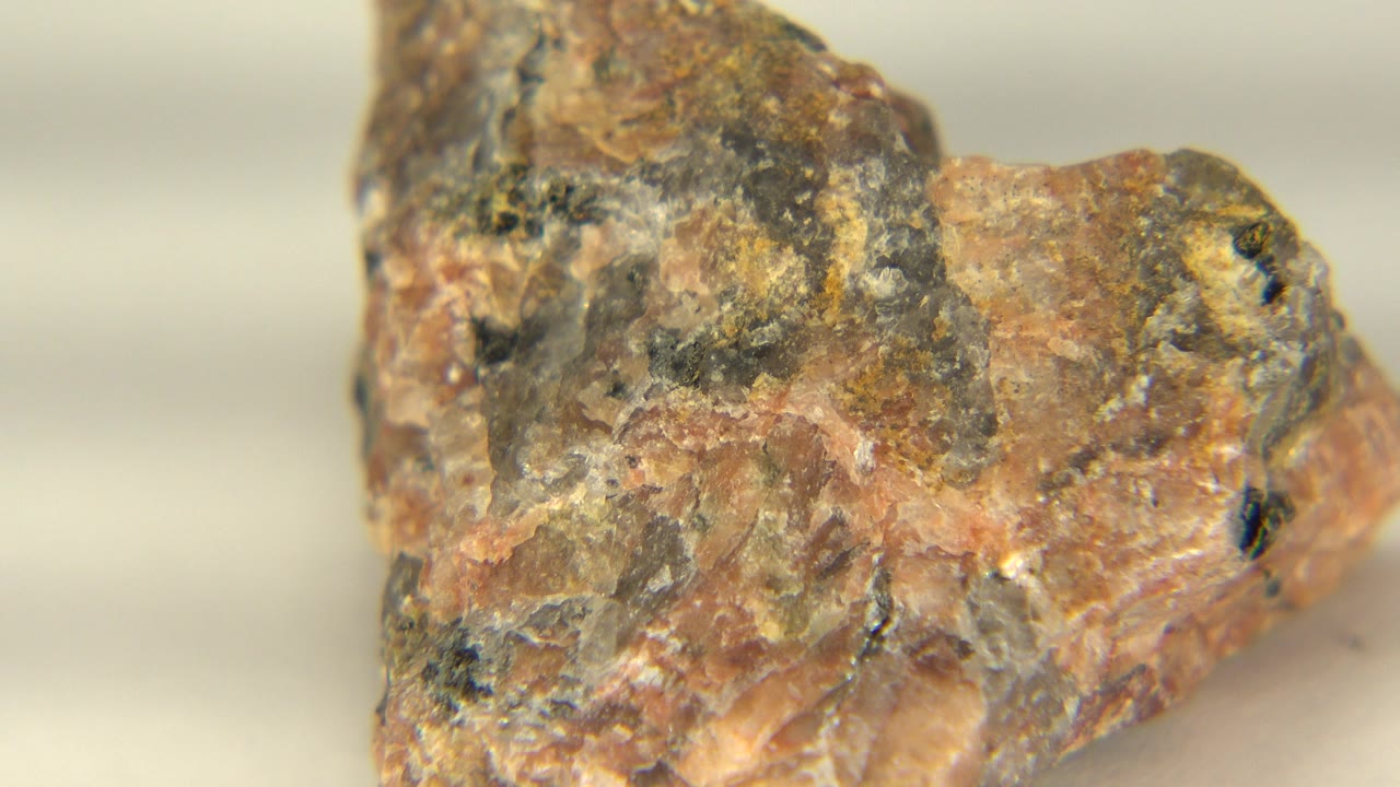 Close-up of a speckled rock on a pale surface in Westminster, Colorado, with tan, gray, white, and dark flecks visible and no visible people.